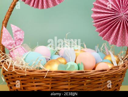 Cesto di vimini con colorate uova di Pasqua in colori pastello e decorato con fiori di carta. Buon biglietto d'auguri pasquale Foto Stock