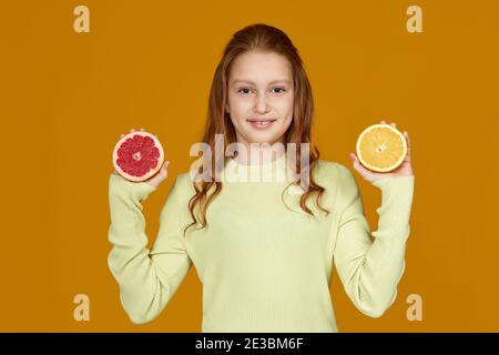 felice bambina rossa che tiene fresco succosa pompelmo e. arancione isolato su sfondo giallo Foto Stock