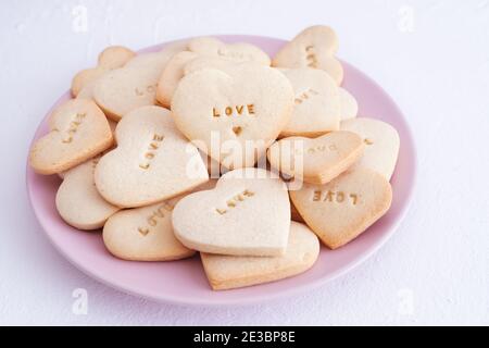 Piatto rosa con biscotti a forma di cuore e parola D'AMORE incisa. Concetto e amore per San Valentino. Foto Stock