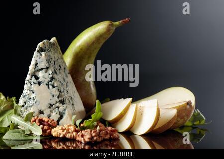 Formaggio blu con noci e pere su sfondo nero riflettente. Spazio di copia. Foto Stock
