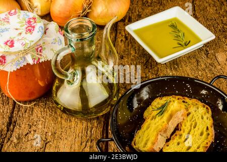 Vaso in vetro d'annata con olio extravergine d'oliva, cipolle e pomodoro conservato su vecchio tavolo di legno. Foto Stock