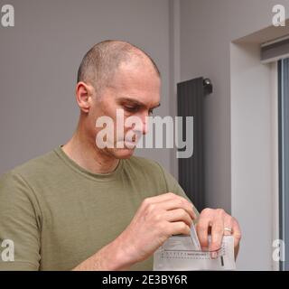 L'uomo che partecipa allo studio di ricerca di covid 19 utilizza un kit di test per la casa, posizionando il campione di tampone nel sacchetto per materiale a rischio biologico. Foto Stock