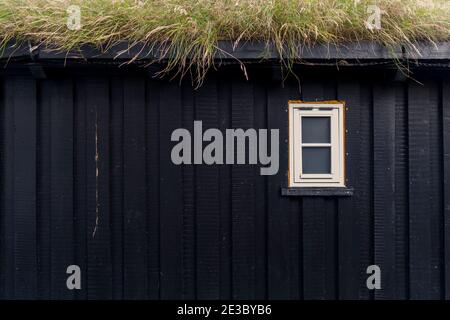 Parete di legno scuro di una piccola casa con una piccola finestra di plastica e tetto erboso. Isole Faroe Foto Stock