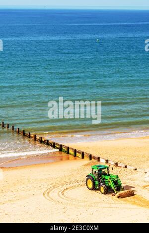 Un trattore che muove la sabbia su una spiaggia inglese in una giornata di sole sullo sfondo bella oceano, industria costiera Foto Stock