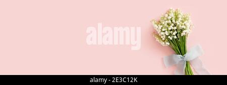Testata con bouquet di giglio dei fiori di valle legati con nastro. Regalo per le madri, giorno delle donne su sfondo rosa. Concetto di primavera con spazio di copia. Foto Stock