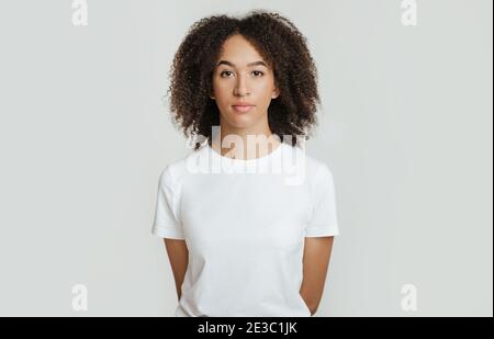 Emozioni gravi, calme, rigide. Emotiva, inemotivamente giovane donna afroamericana tiene le mani dietro di sé Foto Stock