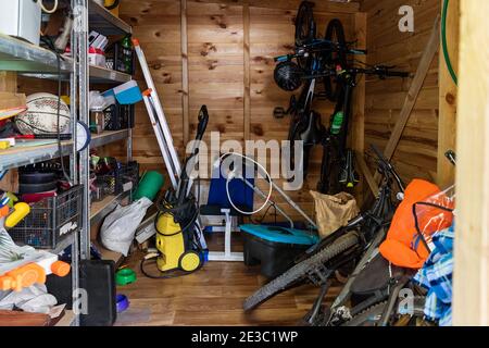 Unità di deposito di utilità di legno della casa suburbana con roba vario su mensole, biciclette, macchina di esercitazione, scala, attrezzi di giardino e attrezzatura. Disordinato Foto Stock