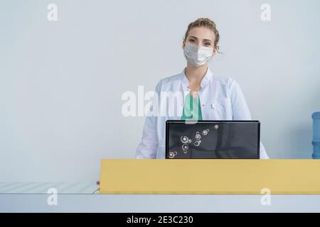 Receptionist femminile che lavora alla scrivania in clinica in maschere di protezione medica. Concetto di prevenzione delle epidemie. Foto Stock