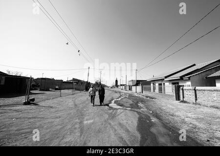 JOHANNESBURG, SUDAFRICA - 05 gennaio 2021: Soweto, Sudafrica - 10 settembre 2011: Due uomini africani che camminano su una strada sterrata di quartiere nel Sowet Foto Stock