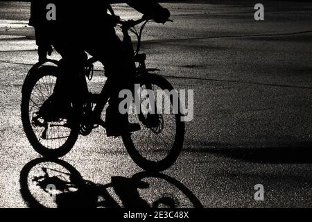 Silhouette nera di un ciclista sulla strada bagnata. Persona che guida una bicicletta, concetto di ciclismo, atmosfera drammatica Foto Stock