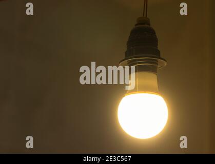 La vecchia lampadina risplende di luce in una stanza buia contro una parete luminosa, dettagli interni Foto Stock
