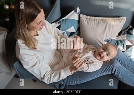 Giovane madre caucasica che si diverte sul divano con il bambino a casa durante la quarantena del coronavirus covid-19. Allontanamento sociale e isolamento di sé. Madre Foto Stock