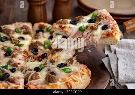 Primo piano di una fetta di pizza con salsiccia, olive nere e peperoni verdi su una spatola da portata Foto Stock