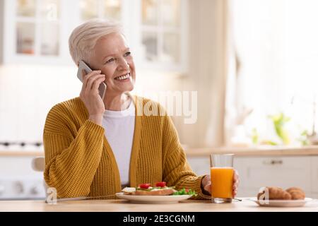 Donna anziana felice che pranza e parla al telefono Foto Stock