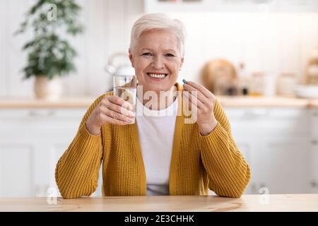 Signora anziana allegra che tiene un bicchiere d'acqua e di pillola Foto Stock