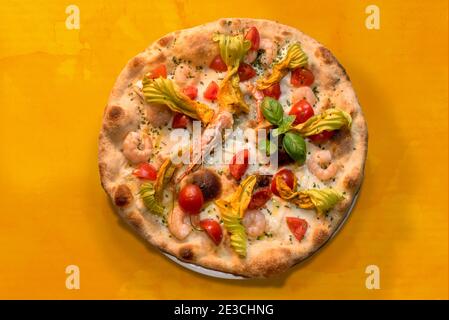 pizza con gamberi, fiori di zucchine, pomodori ciliegini e mozzarella, vista dall'alto piatta su fondo acquerello arancione Foto Stock