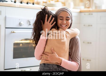 Buon giorno della Madre. Bambina coccolando stretto la sua mamma musulmana in cucina Foto Stock