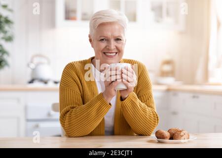 Signora anziana allegra bere tè con croissant Foto Stock