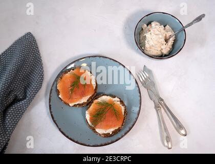 Due fette di pane proteico condite con formaggio cremoso e salmone affumicato su fondo bianco, flatlay, appetitoso, Foto Stock