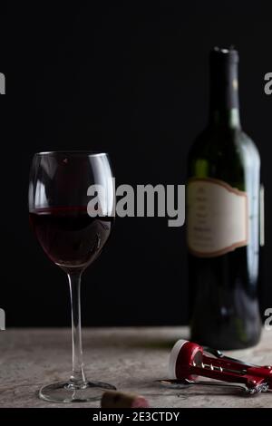 Immagine di un bicchiere di vino di dimensioni standard con vino rosso riempito a metà strada. Sul piano di marmo è presente un cavatappi con un sughero affiancato. Un gr Foto Stock