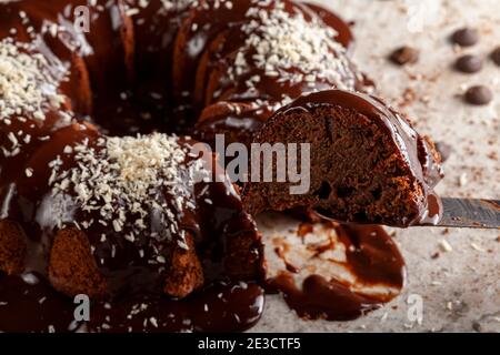 Pronto a mangiare deliziosa torta rotonda al cioccolato con gli shreds di cocco sulla glassa. Un taglio di fetta con una spatola per taglierina a coltello è in fase di rimozione per la manutenzione. Noi Foto Stock