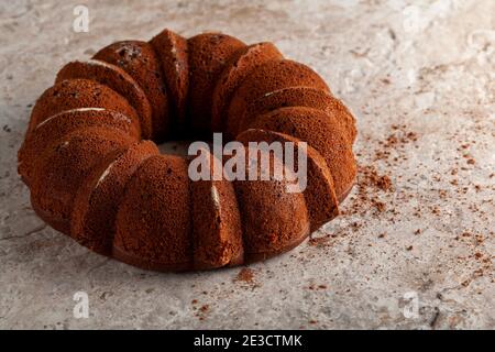 Un pan di Spagna rotondo fresco fuori del forno con i crumbles e le polveri di cacao che rinfrescano sopra un bancone della cucina di marmo o di pietra. L'impressione del ca Foto Stock