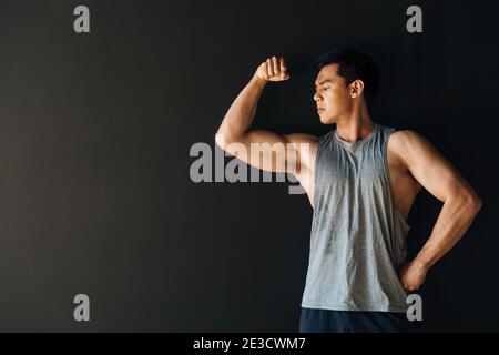 Atleta giovane sano e serio in abbigliamento sportivo che mostra i muscoli delle braccia in studio su sfondo nero Foto Stock