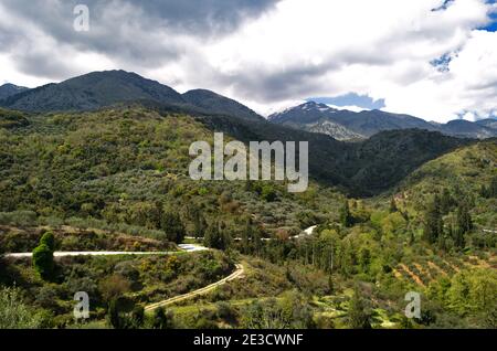Moody paesaggio rurale di oliveti, una strada di campagna tortuosa, e colline a Creta, Grecia Foto Stock