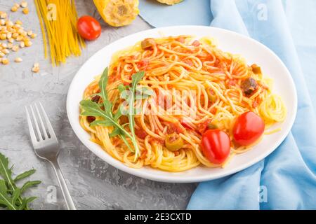 Tagliatelle di mais con salsa di pomodoro e rucola su fondo grigio in cemento e tessuto blu. Vista laterale, primo piano. Foto Stock