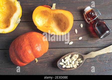 Una bottiglia di olio di semi di zucca, semi di zucca in un cucchiaio di legno e zucche fresche d'autunno su un vecchio tavolo di legno scuro, vista dall'alto Foto Stock