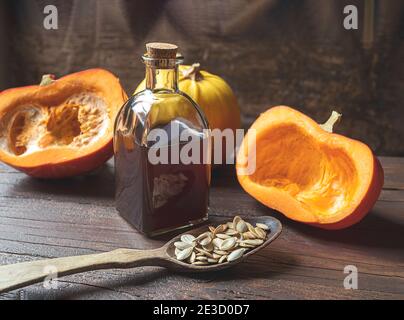 Una bottiglia di olio organico di semi di zucca, semi di zucca in un cucchiaio di legno e zucche d'autunno su un vecchio tavolo di legno scuro Foto Stock