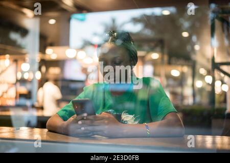 Giovane donna nera autentica seduta con il telefono nel caffè della città negozio Foto Stock