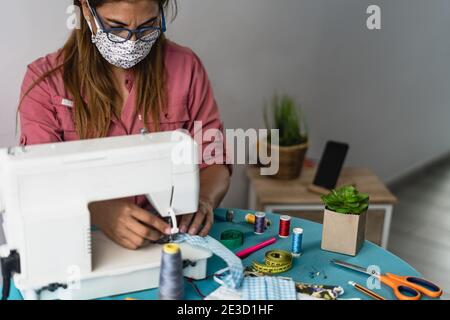 Donna matura che lavora con macchina da cucire facendo maschera fatta in casa per prevenire e fermare la diffusione del virus corona Foto Stock