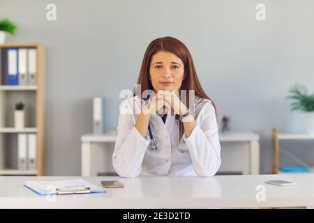 Giovane e sicura dottoressa seduto alla scrivania, guardando la macchina fotografica e ascoltarti Foto Stock