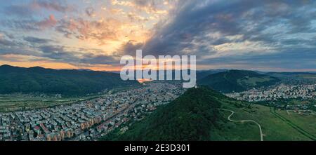 Panorama tramonto sulla verde città di montagna in rumeno Carpazi, paesaggio estivo aereo della città di Piatra Neamt circondata da foresta. Foto Stock