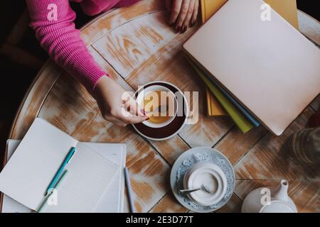 Vista dall'alto di una giovane donna con libro e computer portatile bevanda calda mentre si siede al caffè e si studia Foto Stock