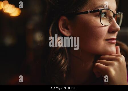 Primo piano di bella donna indossare occhiali e guardare via tenendo la mano sul mento Foto Stock