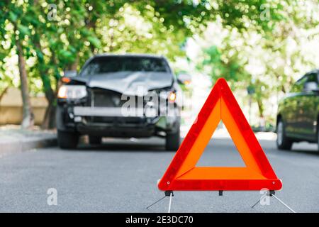 Segnale rosso triangolo di arresto di emergenza sulla strada durante un incidente d'auto. Auto grigia rotta in caso di incidente stradale. Incidente stradale in caso di incidente stradale su strada urbana Foto Stock