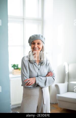 Ritratto di donna anziana con beretto grigio in piedi in casa. Foto Stock