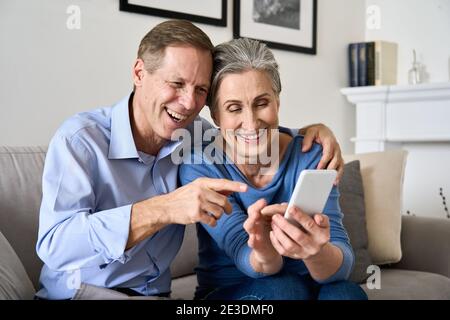 Felice coppia più anziana matura godendo di utilizzare il telefono cellulare seduto sul divano a casa. Foto Stock