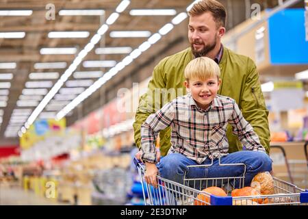 ragazzo ama fare shopping con il padre nel supermercato, bel ragazzo portare il figlio su un carrello, divertirsi Foto Stock