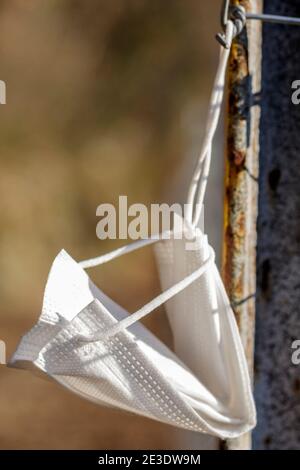 Maschera chirurgica abbandonata su un sentiero di montagna e appesa su un palo da un passante. Foto Stock