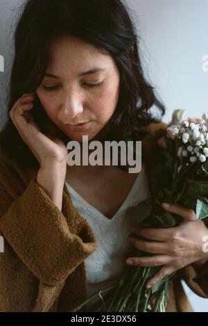 bella giovane donna sorridente che tiene bouquet di primavera colorata a casa su sfondo azzurro. espressione autentica rilassata e aspetto naturale. Foto Stock