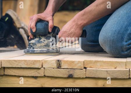 primo piano di un operatore che leviga tavole di legno con un smerigliatrice Foto Stock