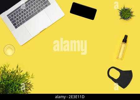 Posto di lavoro con laptop, succulente, telefono, antisettico e maschera su giallo Foto Stock