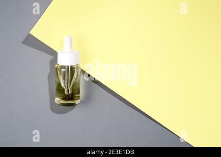 bottiglia cosmetica trasparente flat lay con olio su colore grigio e. sfondo giallo Foto Stock