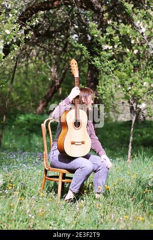 Bionda adolescente attrattiva con la chitarra in giardino primaverile. Foto Stock