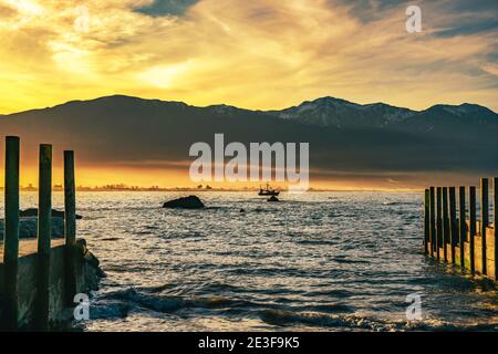 Barca da pesca nella baia di Kaikoura mentre un paesaggio di nuvole di tramonto chiude sulla catena montuosa costiera Foto Stock