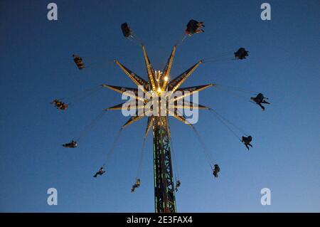 Immagine di silhouette di persone che oscillano in alto nel cielo un giro nel parco divertimenti in serata Foto Stock