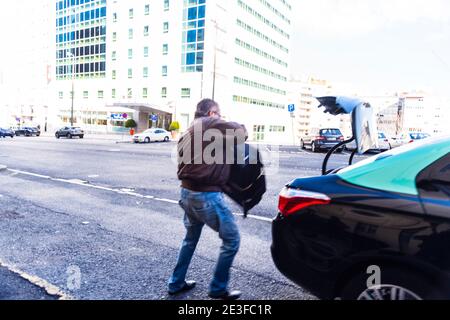 Lisbona, Portogallo - 10 febbraio 2018: Sagoma sfocata del tassista che mette i bagagli duri nel bagagliaio dell'auto vicino all'alto edificio dell'hotel Foto Stock